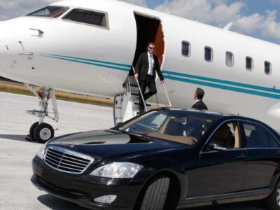 a person coming out of small plane and hired airport limo car with chauffeur is there to receive him