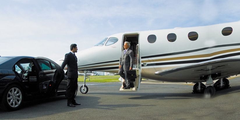 a person is coming out of a plane and a chauffeur is holding the door of a limousine for him