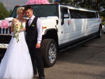 a newly married couple standing in front of a white hummer limousine for their wedding event
